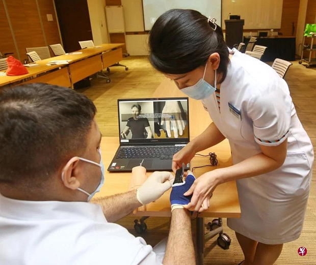 ​中央医院护士长曹兆琳（右）为护士戴尔星（Dyal Singh）戴上装有压力传感器的手套，准备为虚拟病患进行静脉插管。（特约陈福洲摄）